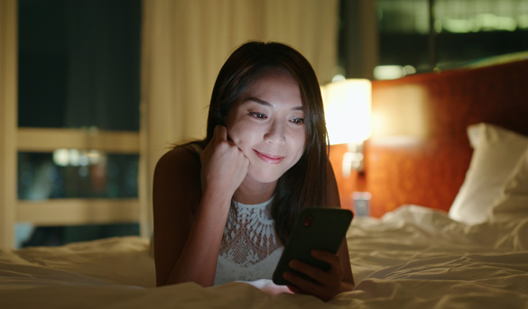 femme sur un lit d'hôtel au téléphone connecté en wifi